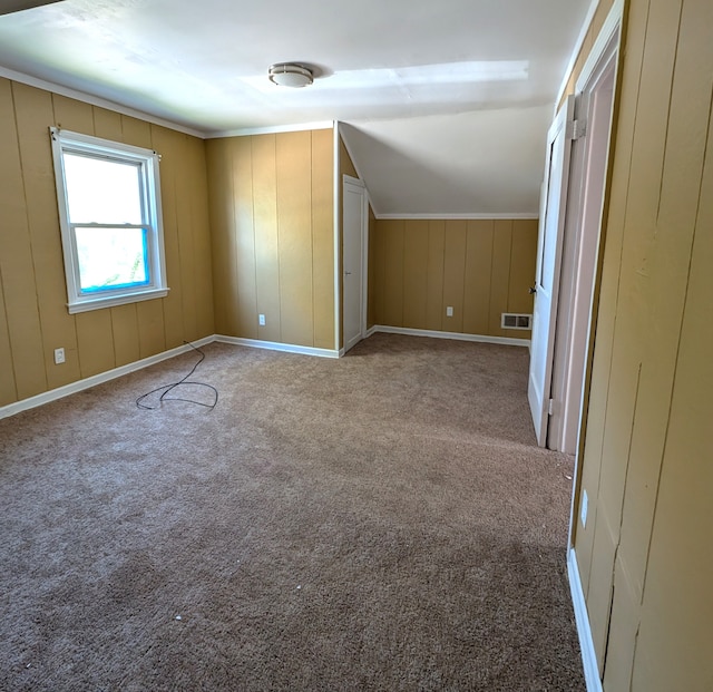 additional living space with light colored carpet, lofted ceiling, and wood walls