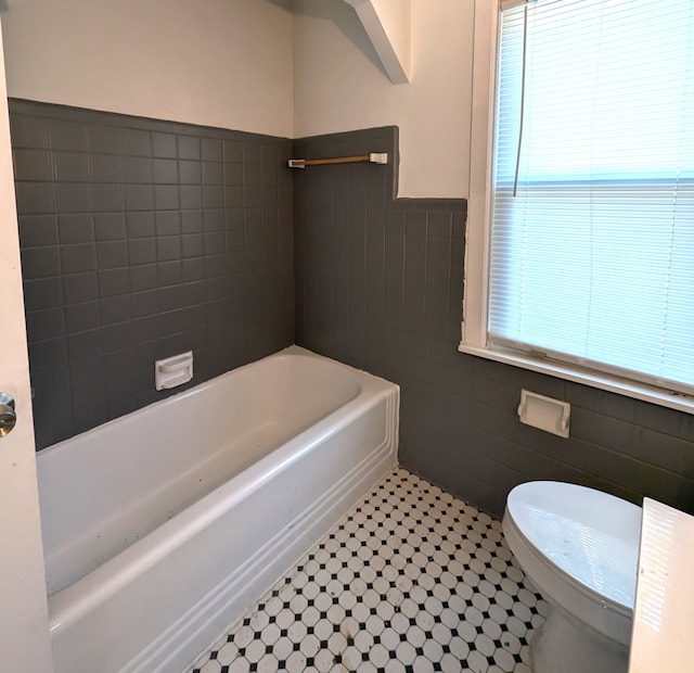 bathroom featuring tile patterned flooring, a washtub, toilet, and tile walls