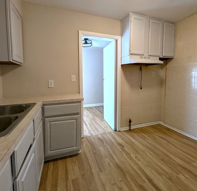 kitchen featuring white cabinets, sink, light wood-type flooring, and tile walls