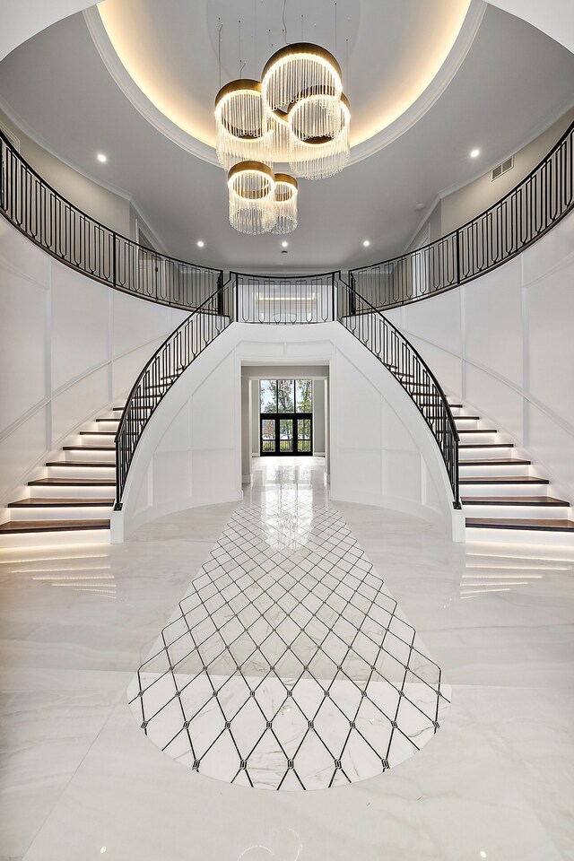 stairs with a notable chandelier, a high ceiling, and a tray ceiling