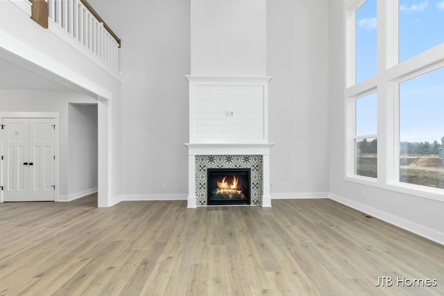 unfurnished living room with a tiled fireplace, a towering ceiling, and light hardwood / wood-style floors