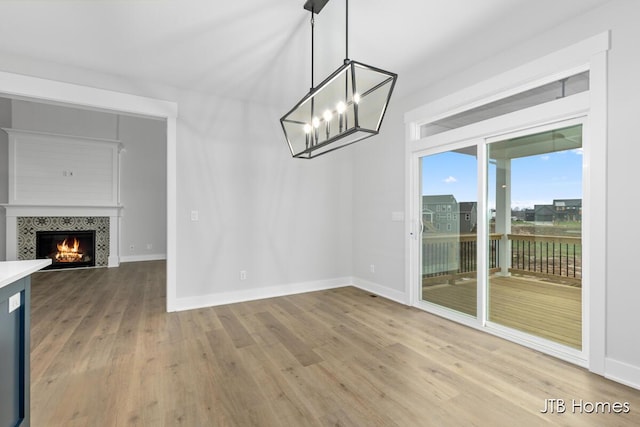 unfurnished dining area with hardwood / wood-style flooring, an inviting chandelier, and a tile fireplace