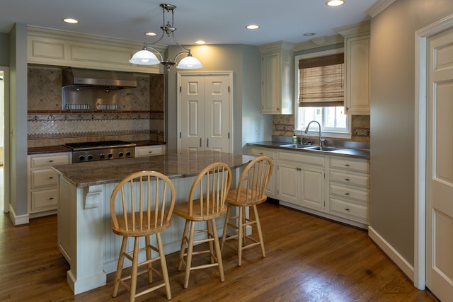 kitchen featuring a kitchen bar, sink, hanging light fixtures, a kitchen island, and dark hardwood / wood-style flooring