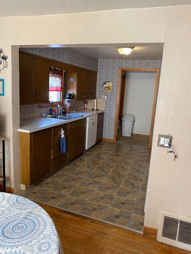 kitchen featuring backsplash, dark brown cabinetry, white dishwasher, sink, and dark hardwood / wood-style floors