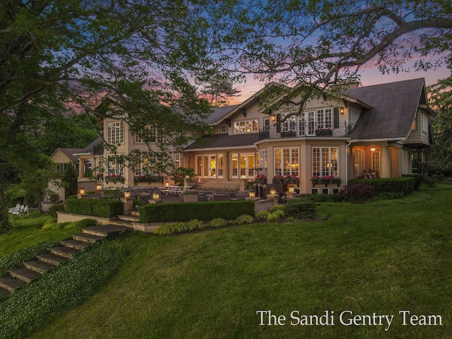 back house at dusk with a lawn, a patio, and french doors