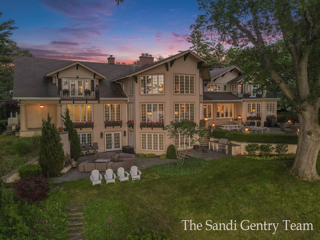 back house at dusk with a patio area, a yard, a balcony, and french doors