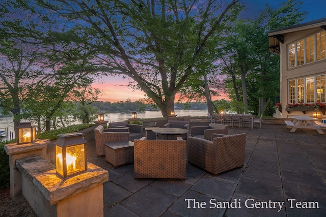 patio terrace at dusk featuring a water view and an outdoor living space with a fire pit