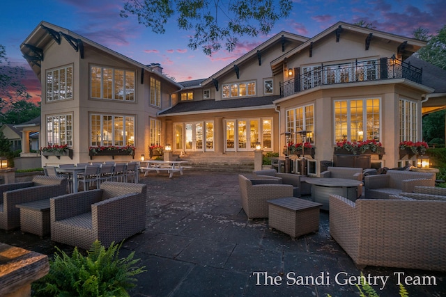 back house at dusk featuring a patio area, a balcony, and an outdoor hangout area