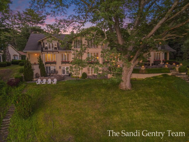 18635 N Fruitport Rd, Spring Lake, MI 49456 - back of property at dusk featuring french doors, stucco siding, a patio, and a lawn