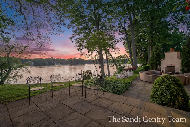 patio terrace at dusk with a water view and exterior fireplace