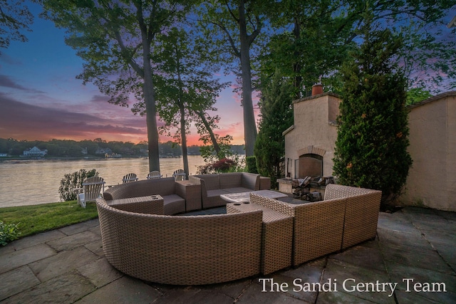 patio terrace at dusk featuring an outdoor living space with a fireplace and a water view