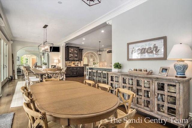 dining area featuring a chandelier, indoor bar, dark wood-type flooring, and crown molding