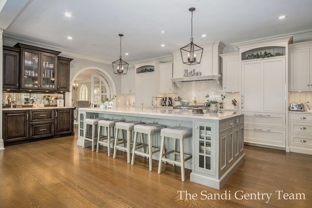 kitchen with dark wood-type flooring, a spacious island, decorative light fixtures, a kitchen bar, and dark brown cabinetry