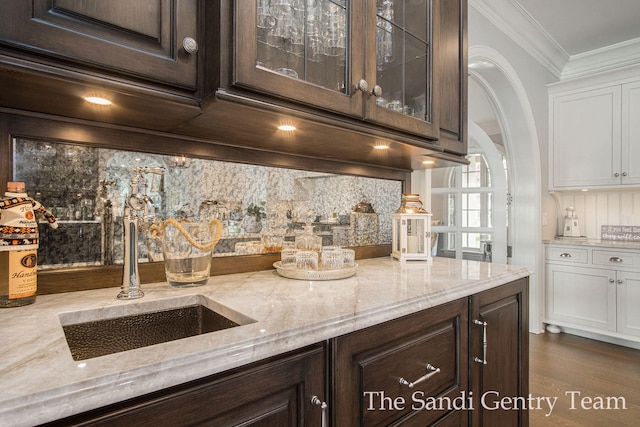 kitchen featuring dark brown cabinetry, light stone countertops, sink, and ornamental molding