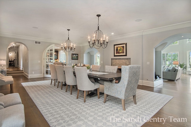 dining space featuring a brick fireplace, crown molding, wood-type flooring, and a notable chandelier