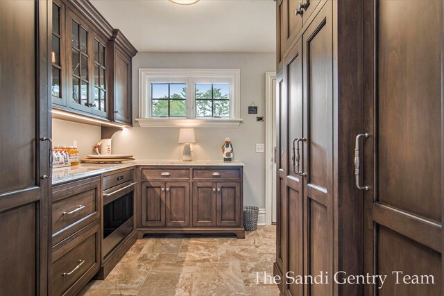 18635 N Fruitport Rd, Spring Lake, MI 49456 - kitchen featuring light countertops, dark brown cabinetry, glass insert cabinets, light stone finish flooring, and an office area
