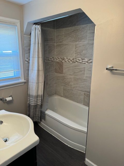 bathroom featuring wood-type flooring, shower / bathtub combination with curtain, and sink