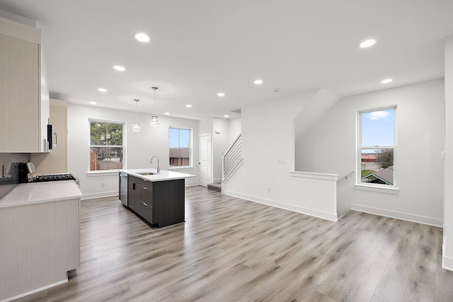 kitchen featuring sink, an island with sink, decorative light fixtures, light hardwood / wood-style floors, and stainless steel appliances