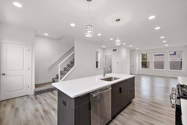 kitchen featuring appliances with stainless steel finishes, sink, decorative light fixtures, light hardwood / wood-style floors, and an island with sink