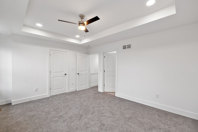 unfurnished bedroom featuring a tray ceiling, ceiling fan, carpet, and two closets