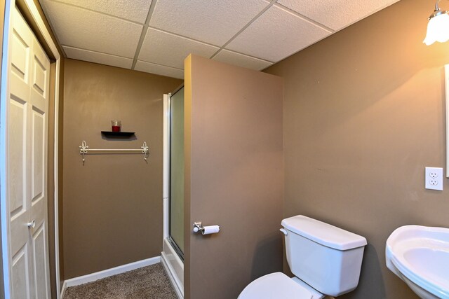 bathroom featuring a drop ceiling, toilet, sink, and walk in shower