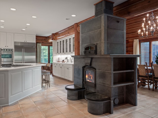 kitchen featuring a wood stove, white cabinetry, light tile patterned floors, and appliances with stainless steel finishes