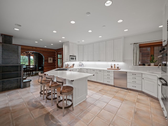 kitchen featuring white cabinets, stainless steel dishwasher, a kitchen bar, and white microwave