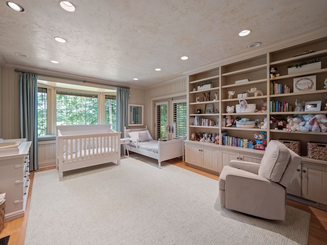 bedroom featuring light wood-type flooring, a crib, french doors, and multiple windows