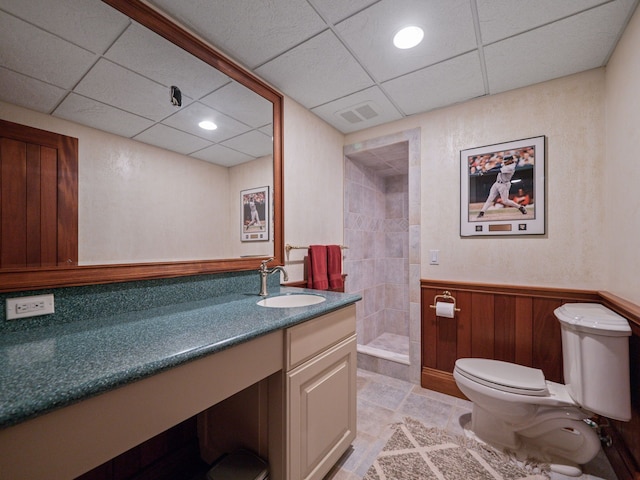 bathroom featuring a paneled ceiling, walk in shower, vanity, wooden walls, and toilet