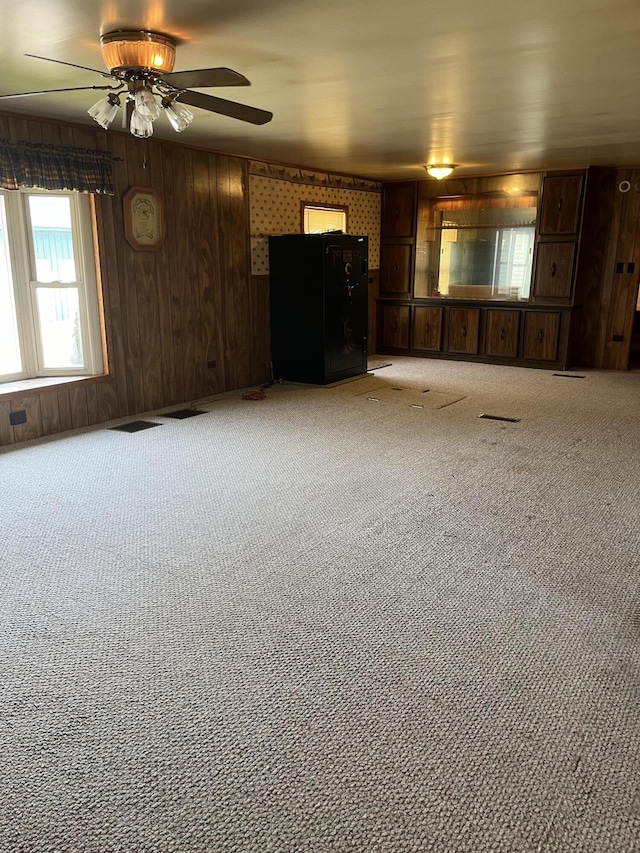 unfurnished living room featuring light carpet, ceiling fan, and wood walls