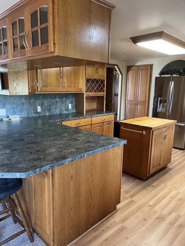 kitchen featuring kitchen peninsula, stainless steel fridge with ice dispenser, light hardwood / wood-style floors, and decorative backsplash