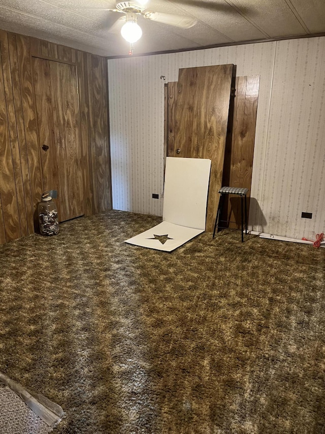 empty room featuring carpet, ceiling fan, wood walls, and a textured ceiling