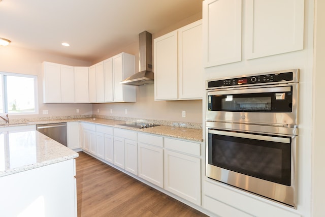 kitchen featuring stainless steel appliances, wall chimney exhaust hood, light wood-type flooring, and white cabinetry