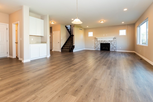 unfurnished living room featuring stairs, baseboards, a fireplace, and wood finished floors