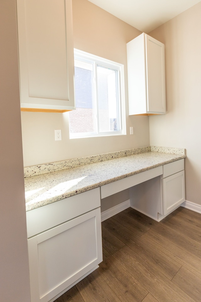 kitchen featuring dark wood-style flooring, built in desk, white cabinets, light stone countertops, and baseboards