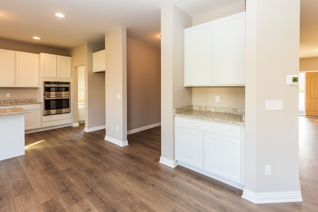 kitchen featuring double oven, white cabinetry, light stone counters, and dark wood-style floors