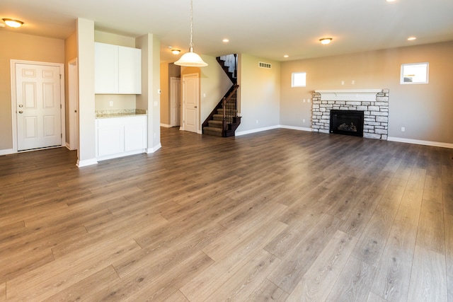 unfurnished living room featuring baseboards, visible vents, stairway, wood finished floors, and a stone fireplace