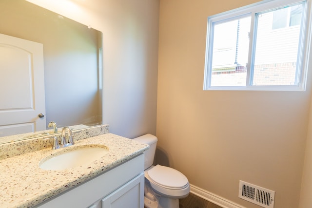 half bathroom featuring baseboards, visible vents, vanity, and toilet