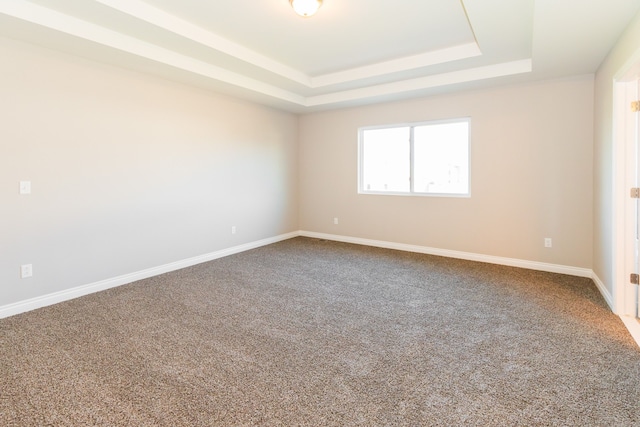 empty room with carpet floors, a tray ceiling, and baseboards