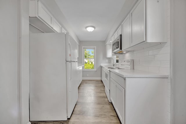 kitchen with backsplash, white appliances, sink, light hardwood / wood-style floors, and white cabinetry