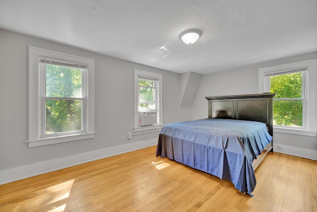 bedroom with a textured ceiling, light hardwood / wood-style flooring, and cooling unit