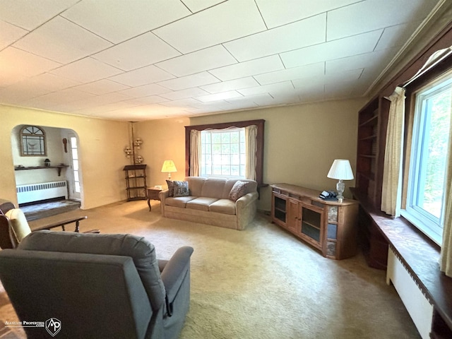 carpeted living room with plenty of natural light, radiator, and arched walkways