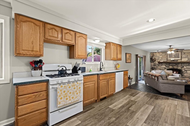 kitchen featuring dark hardwood / wood-style flooring, white appliances, ceiling fan, sink, and a fireplace