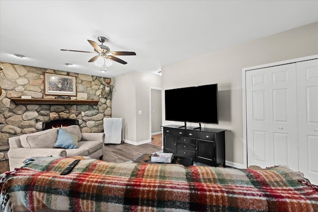 living room featuring hardwood / wood-style flooring, a stone fireplace, and ceiling fan