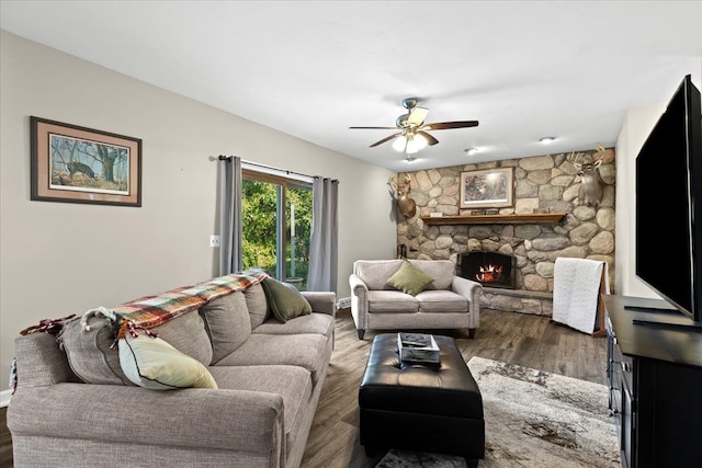 living room with a stone fireplace, ceiling fan, and dark wood-type flooring