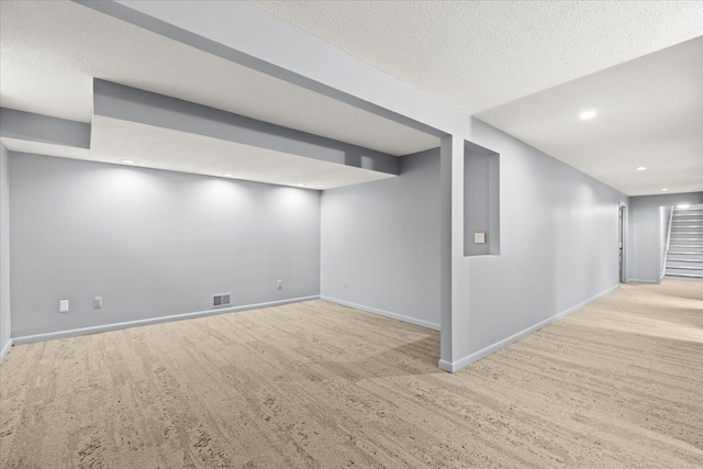 basement featuring light carpet and a textured ceiling