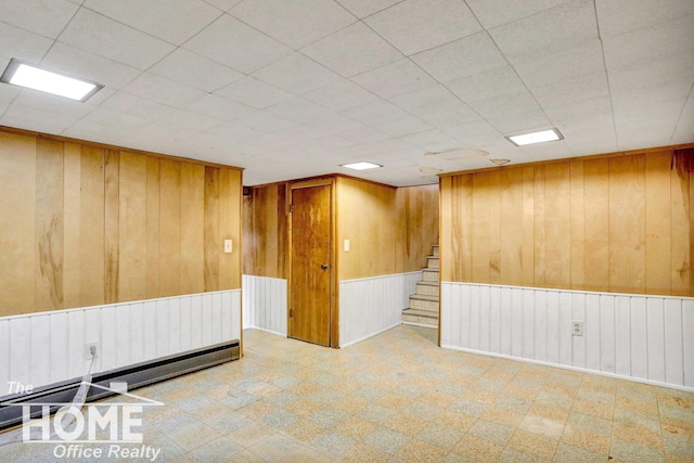 unfurnished room featuring tile patterned floors, stairway, baseboard heating, and wooden walls