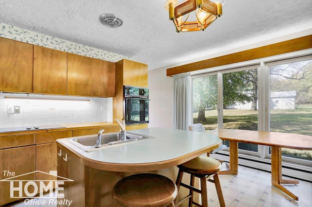 kitchen featuring sink, a breakfast bar area, a center island with sink, black oven, and decorative backsplash