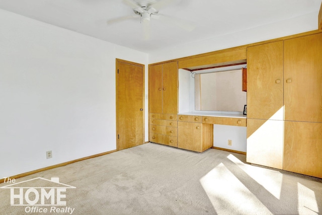 unfurnished bedroom with baseboards, light carpet, a ceiling fan, and built in study area