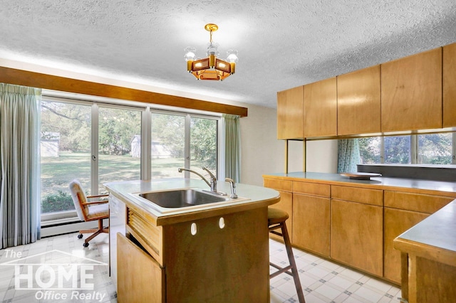 kitchen featuring a kitchen bar, sink, decorative light fixtures, a center island with sink, and a textured ceiling